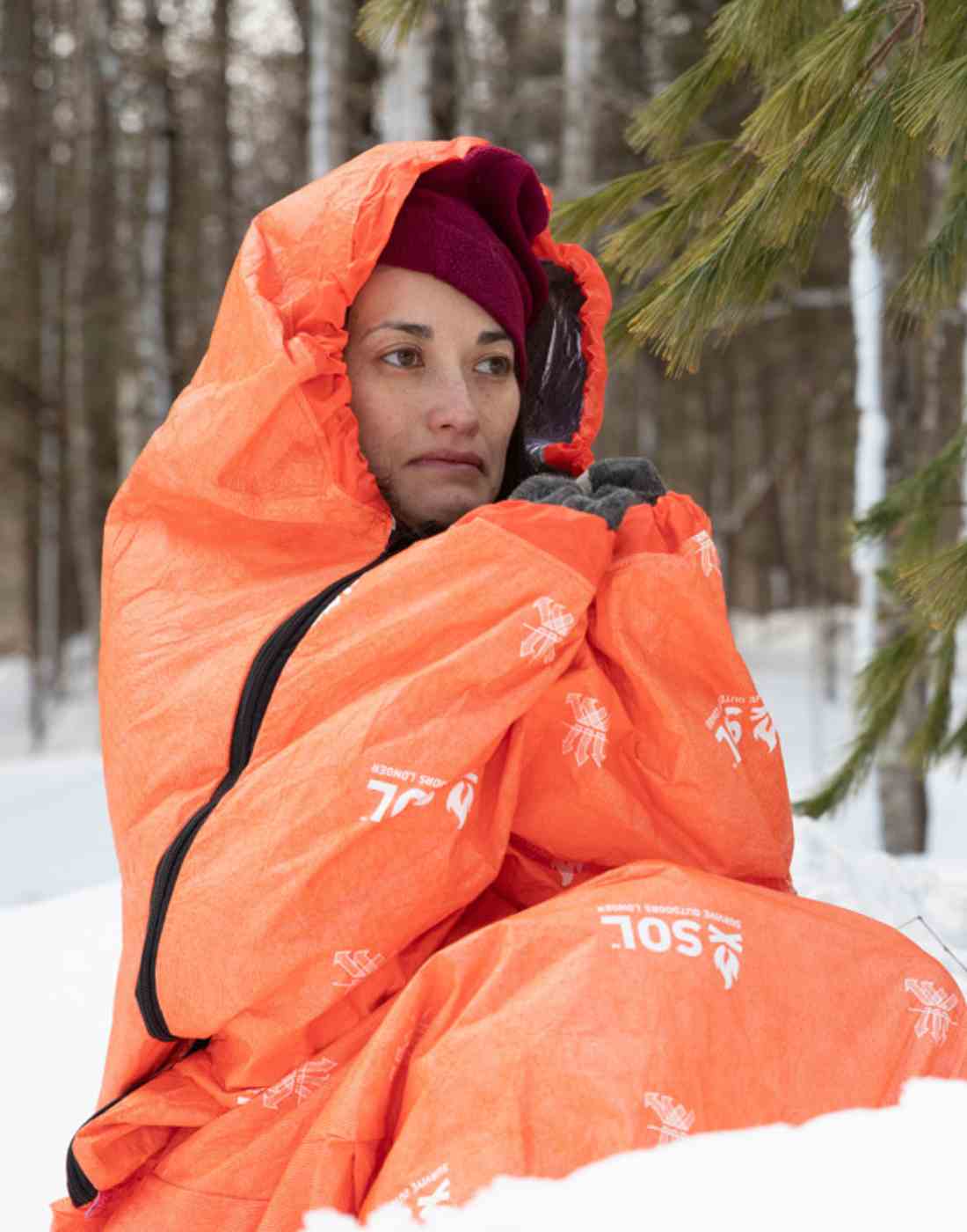 Woman with Hat Sitting in Snow in Orange SOL Escape Bivvy