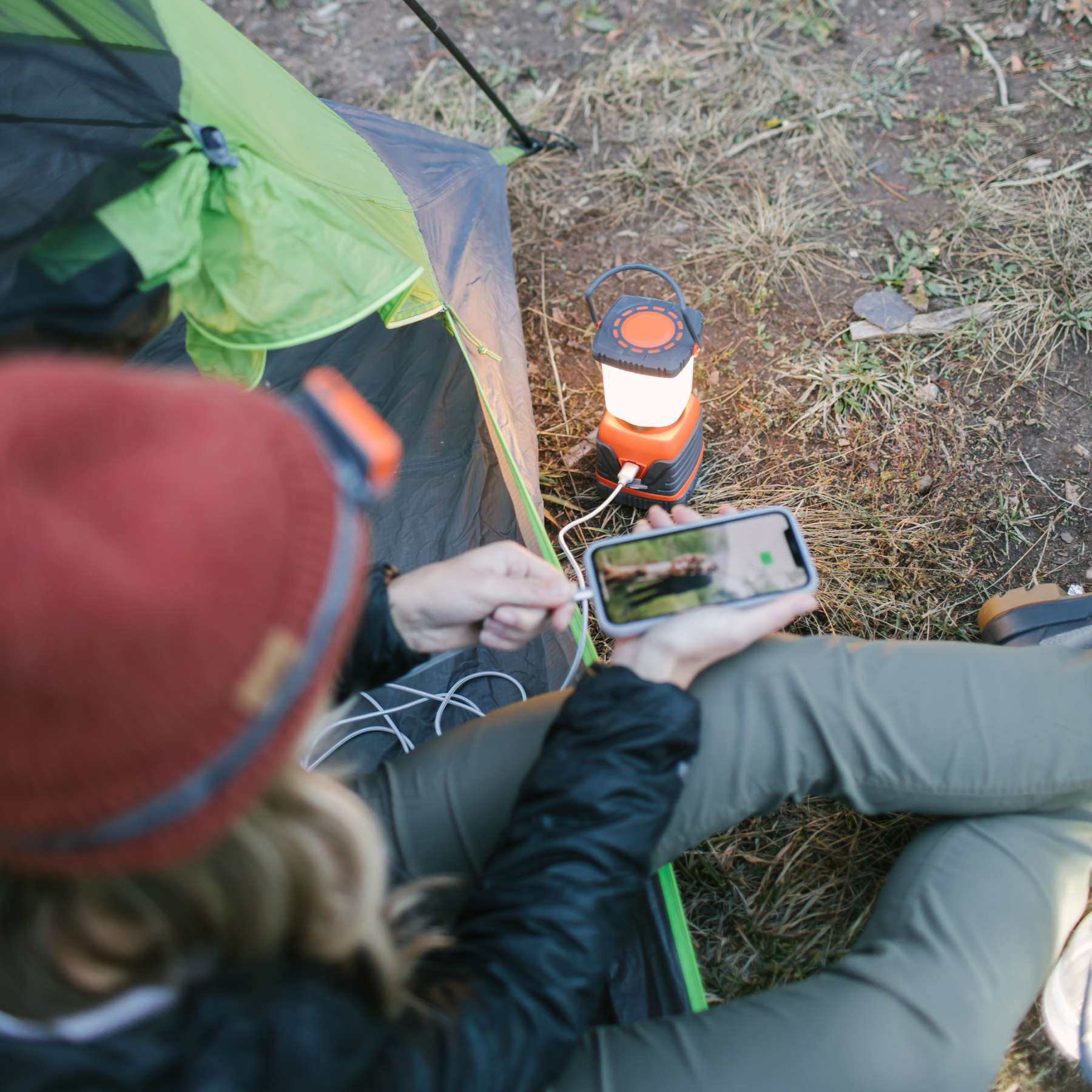 Woman Sitting in Tent Charging Phone with SOL Rechargeable Camp Lantern Power Bank