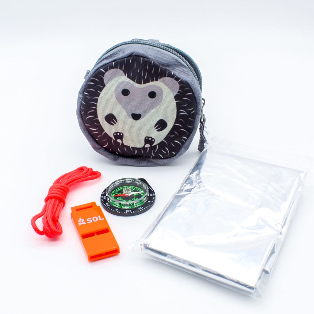 Camp Critter Kit Hedgehog with contents laid in front of it - compass, tinder cord, whistle and emergency blanket