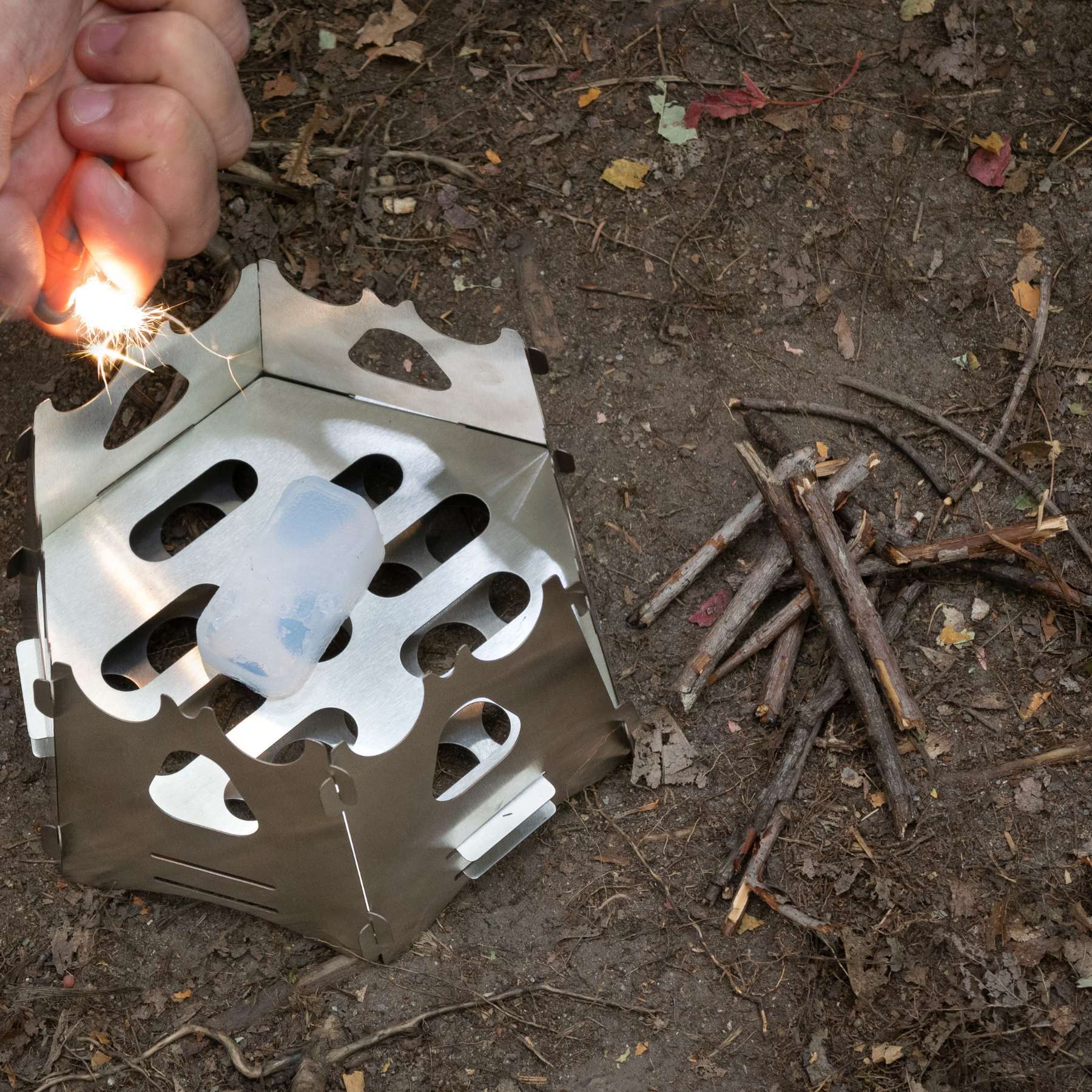 Person Lighting SOL Fire Cubes in Backpacking Stove on Dirt Ground