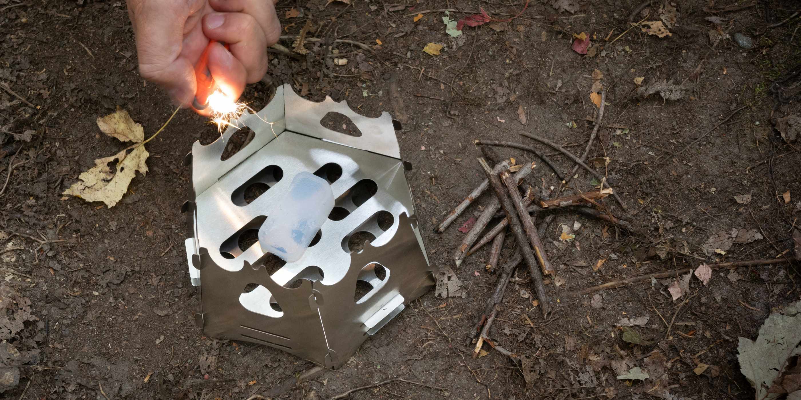 Person Lighting SOL Fire Cubes in Backpacking Stove on Dirt Ground