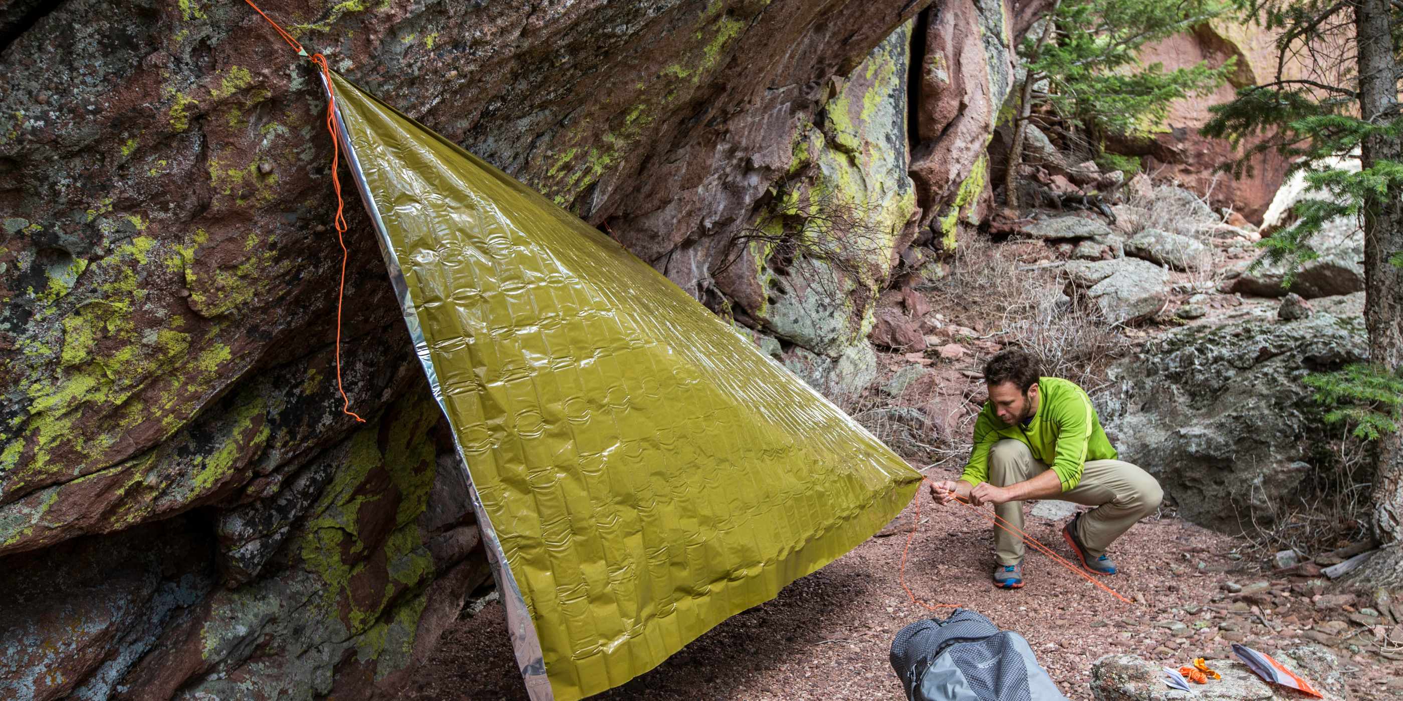 Man Rigging Green SOL Heavy Duty Emergency Blanket as a Shelter on a Large Rock