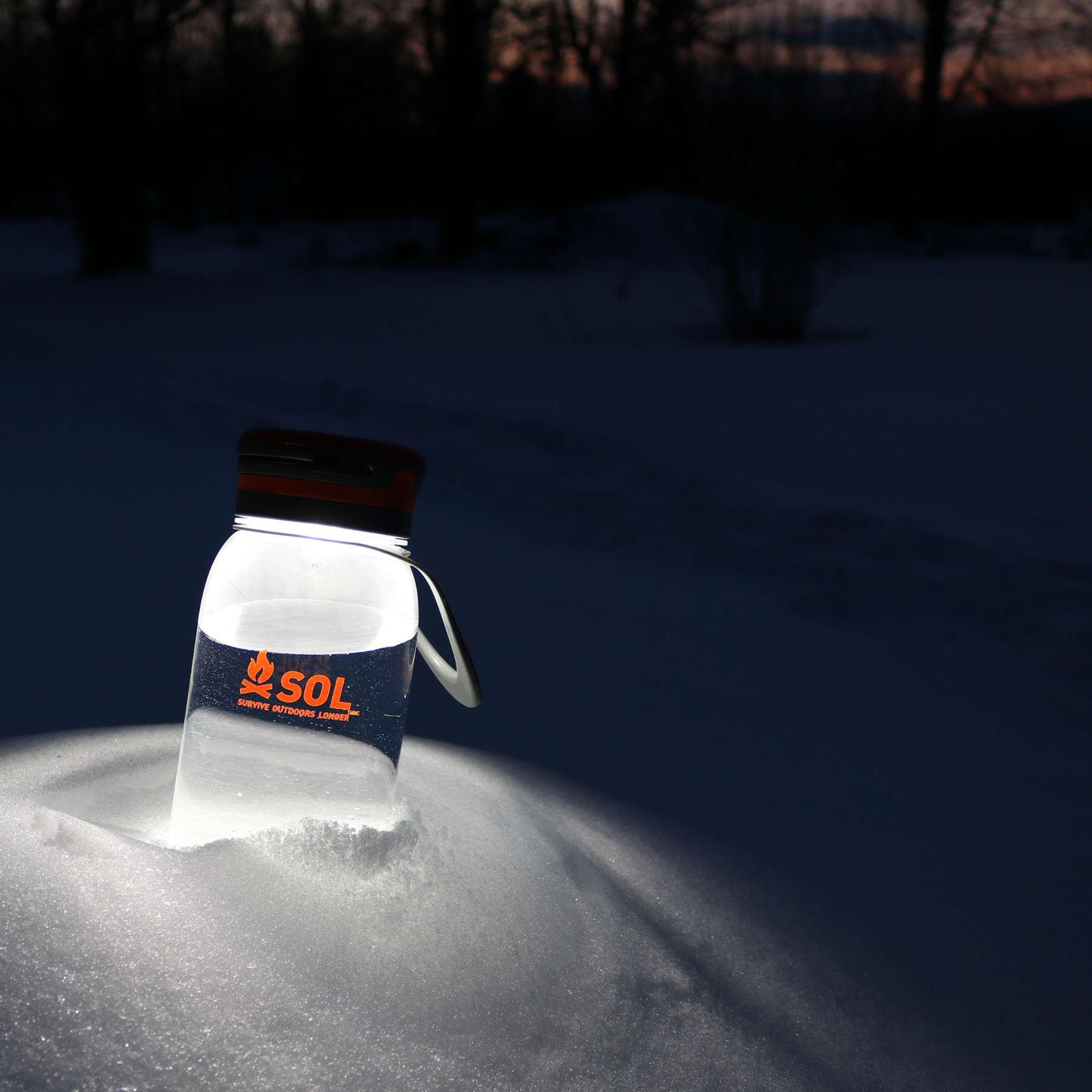 SOL Solar Water Bottle Lantern Lit Sitting in Snow in Darkness