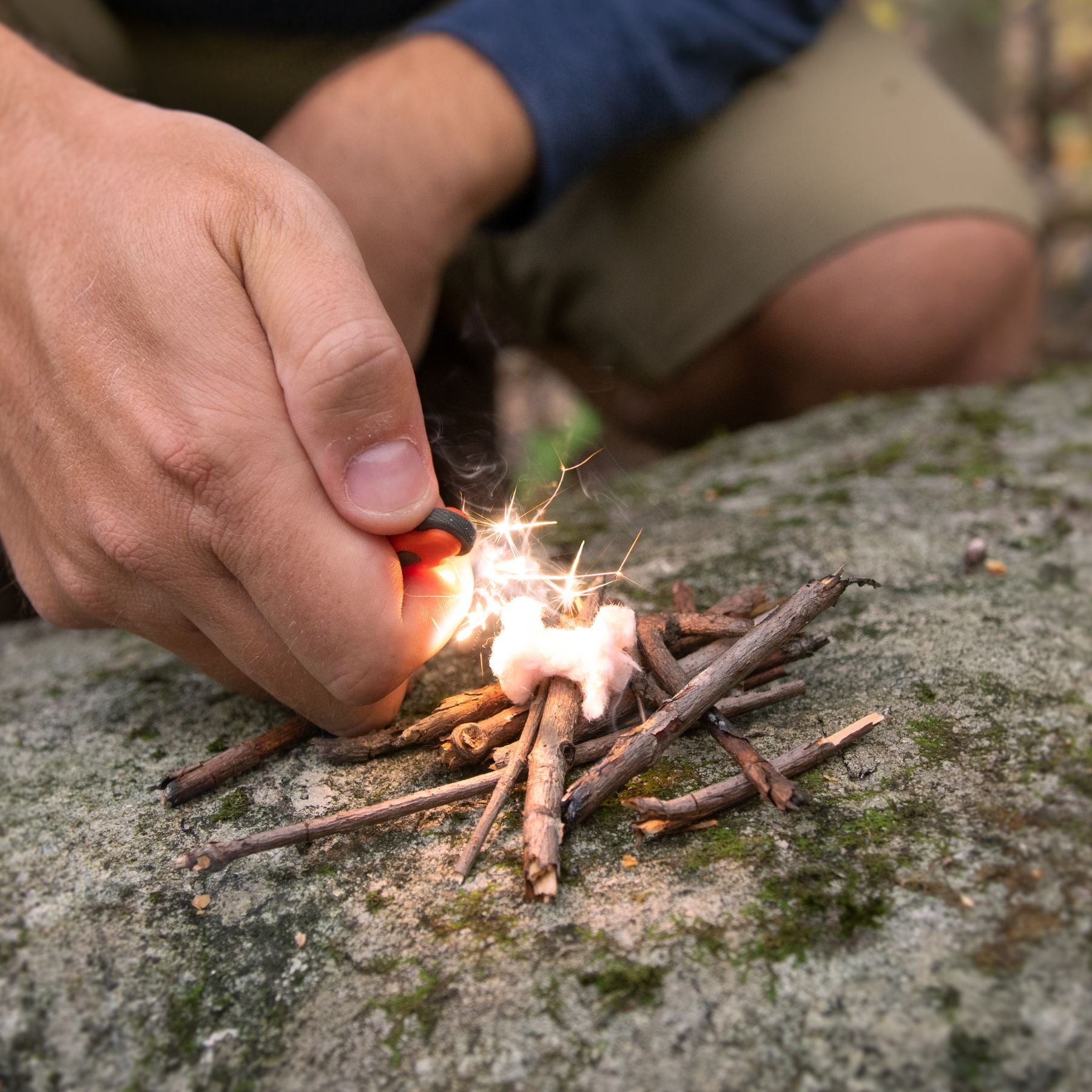 Person Lighting Tinder Quik on Rock with Twigs