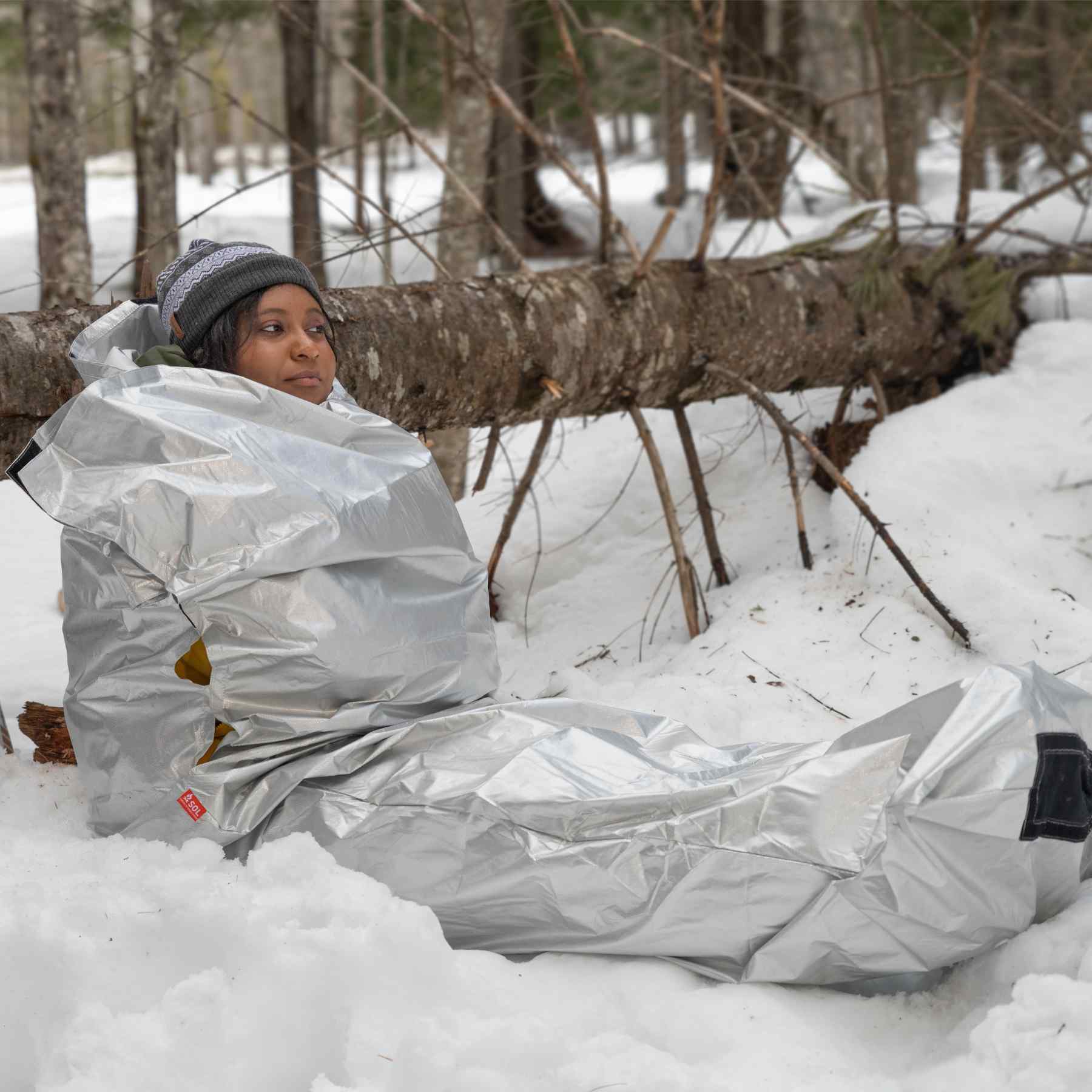 Thermal Bivvy with Rescue Whistle woman laying in bivvy leaning on log while in snow