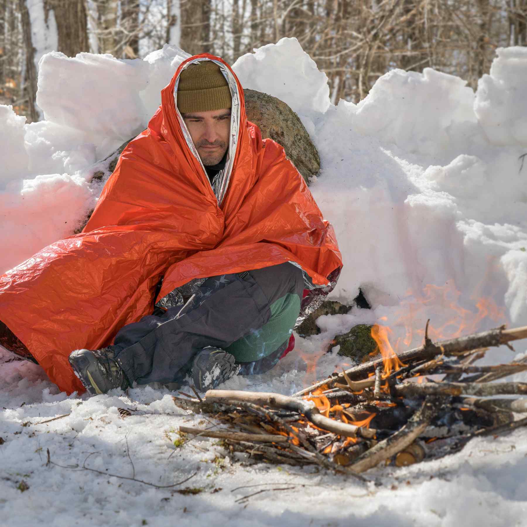 Emergency Blanket man wrapped in blanket in snow in front of fire