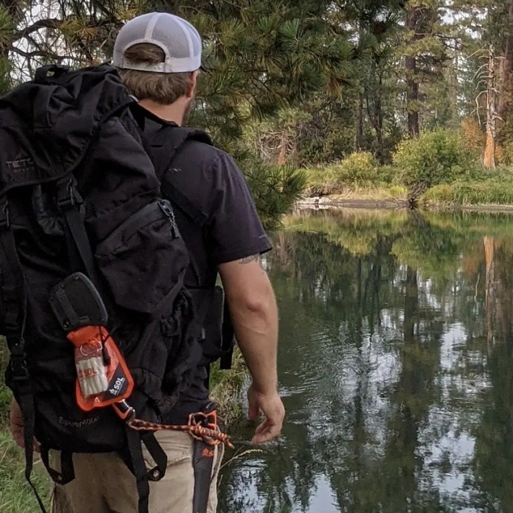 Fire Lite Kit in Dry Bag man with kit attached to black backpack while standing in front of pond
