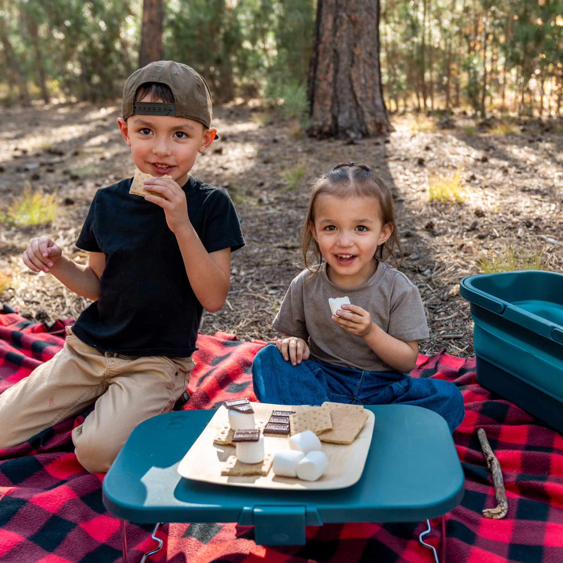 Two kids eating s'mores at a camp site from the table top lid of the Adventure Ready Picnic Basket.