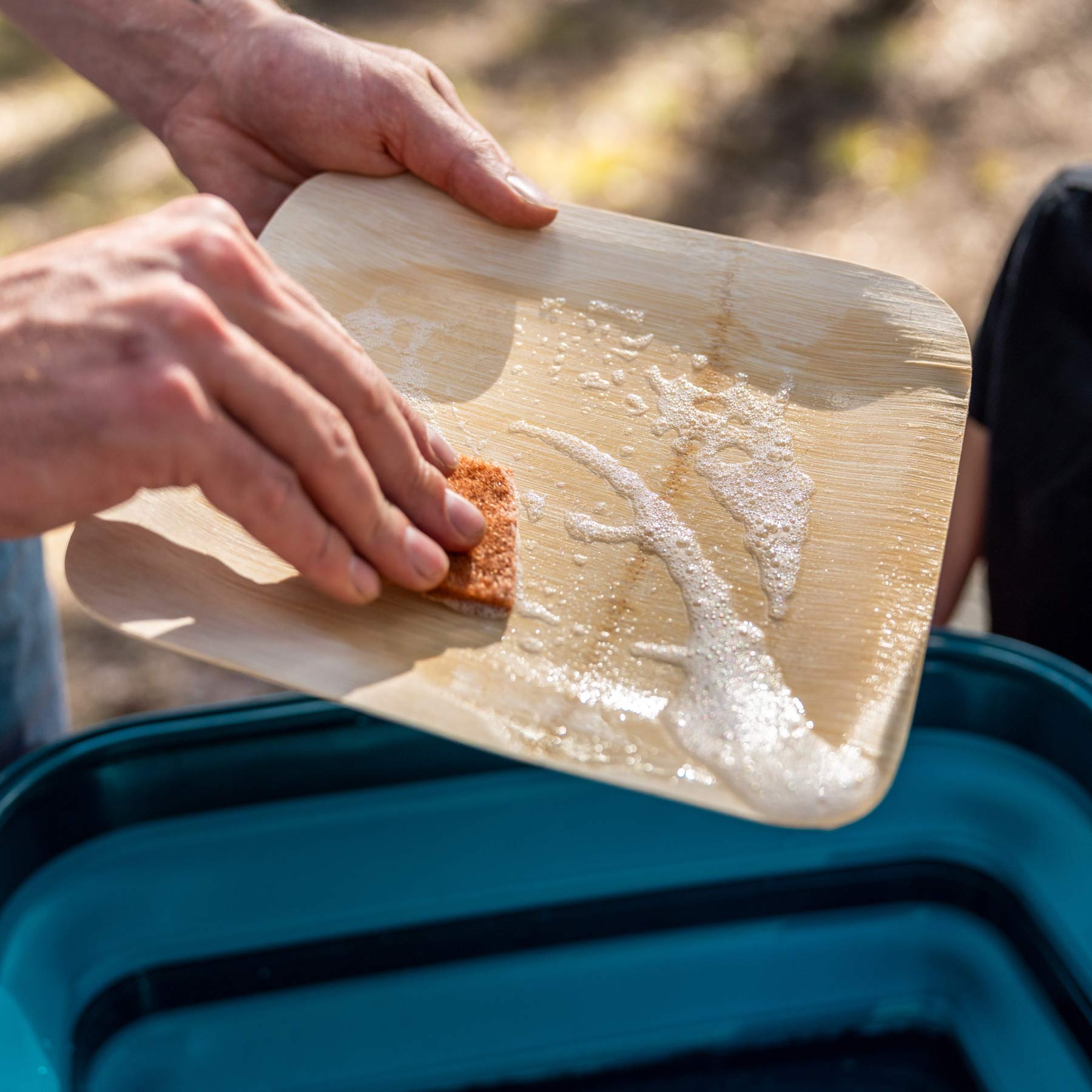 Image shows a person washing their bamboo plate with the coconut scrubber over the AR Sink 16L.