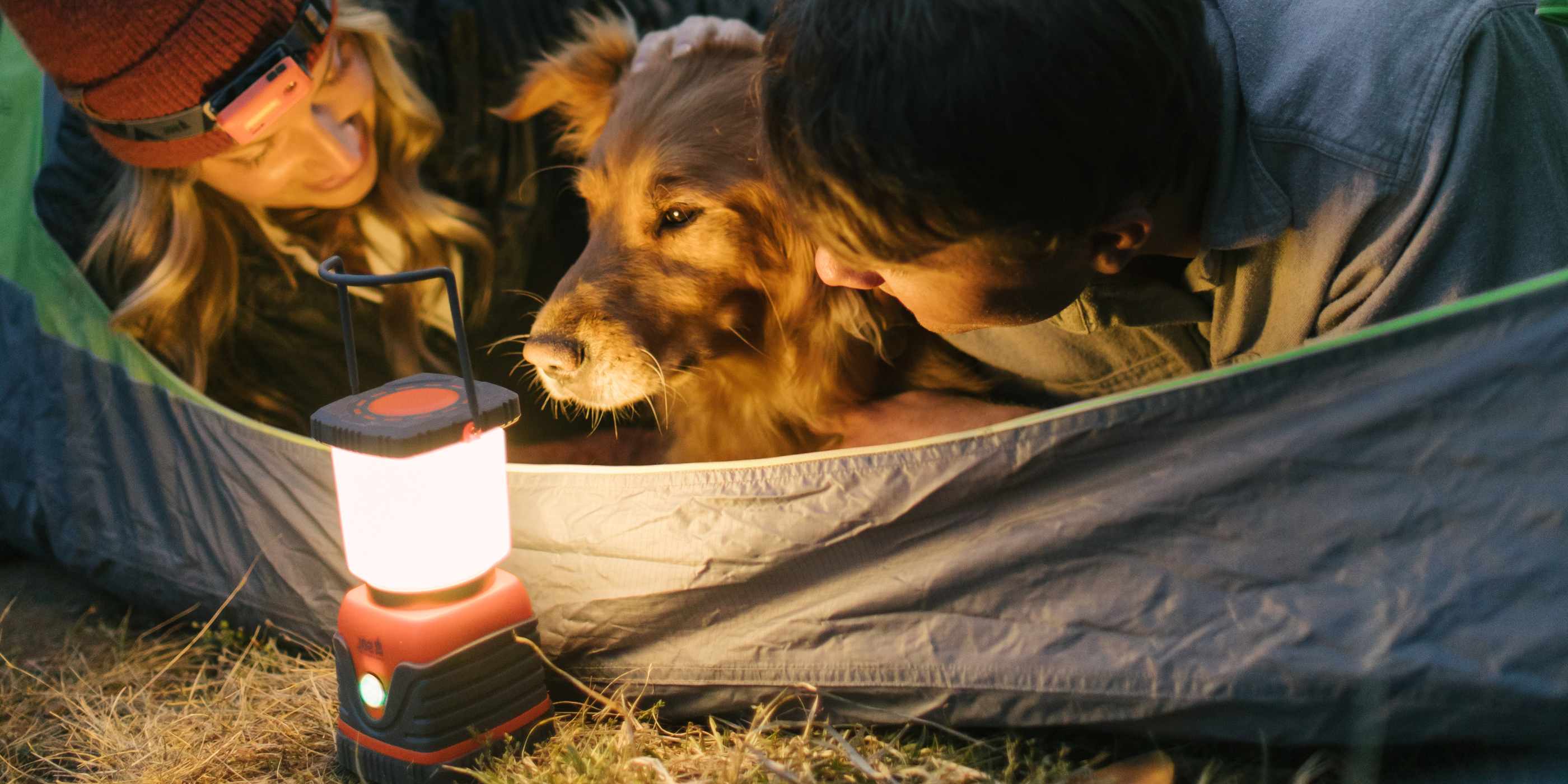 SOL Camping Lantern Lit in Front of Open Tent with Golden Retriever and Woman in Tent