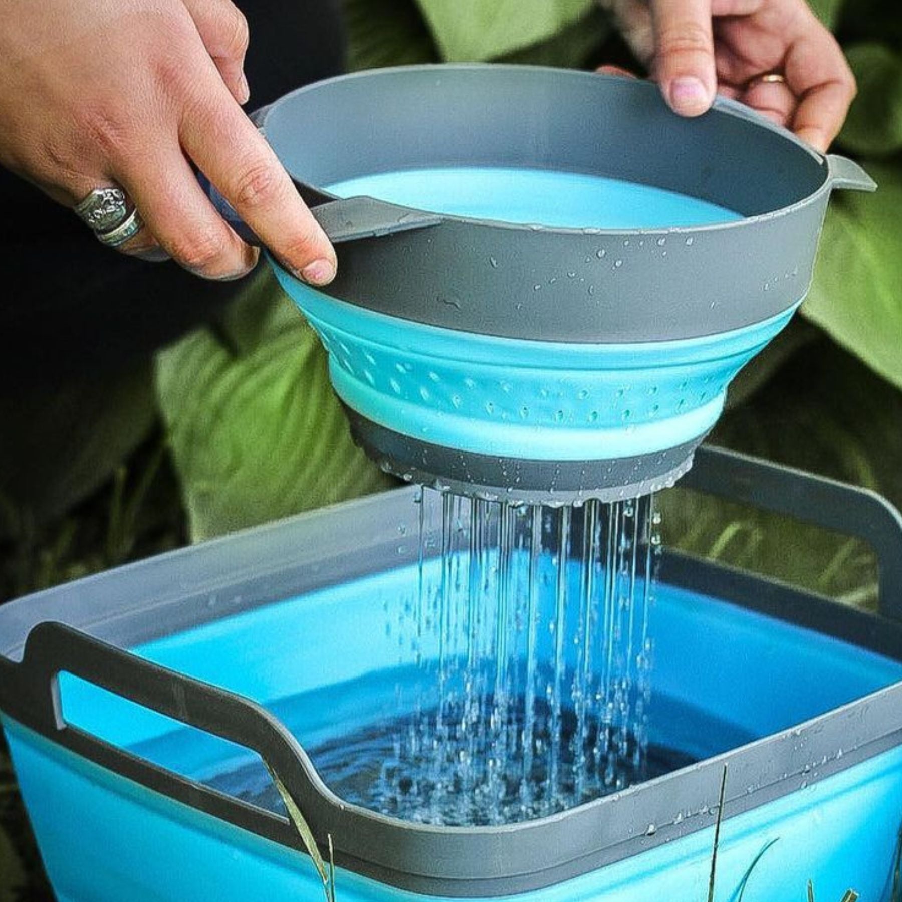 Person Using Blue and Gray SOL Collapsible Strainer Straining Water in Front of Large Green Leaves