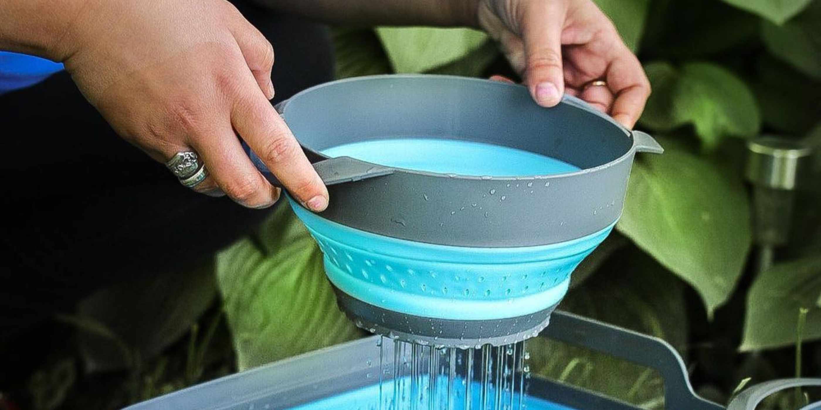 Person Using Blue and Gray SOL Collapsible Strainer Straining Water in Front of Large Green Leaves
