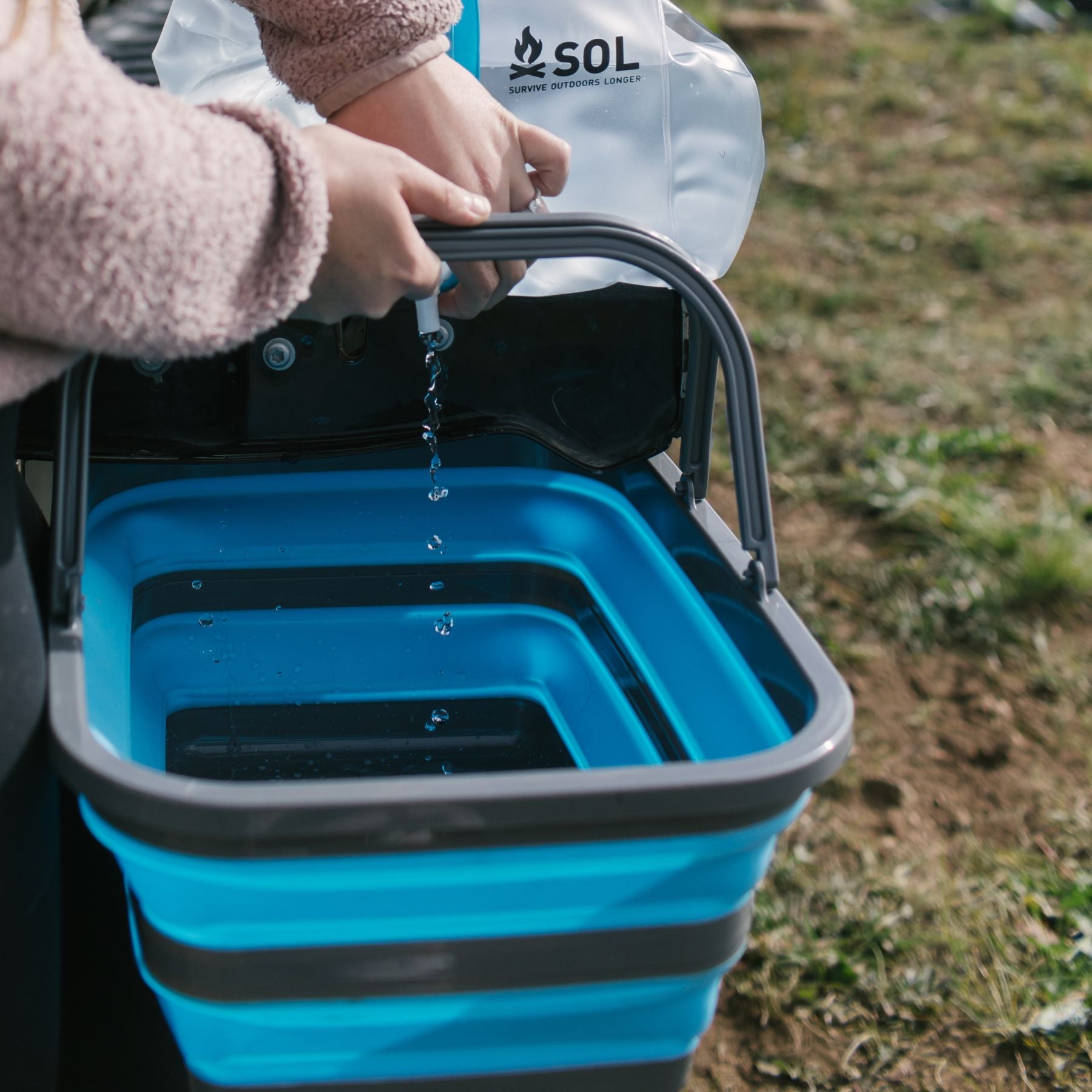 Woman Pouring Water into Blue and Gray SOL Flat Pack Collapsible Sink 16L