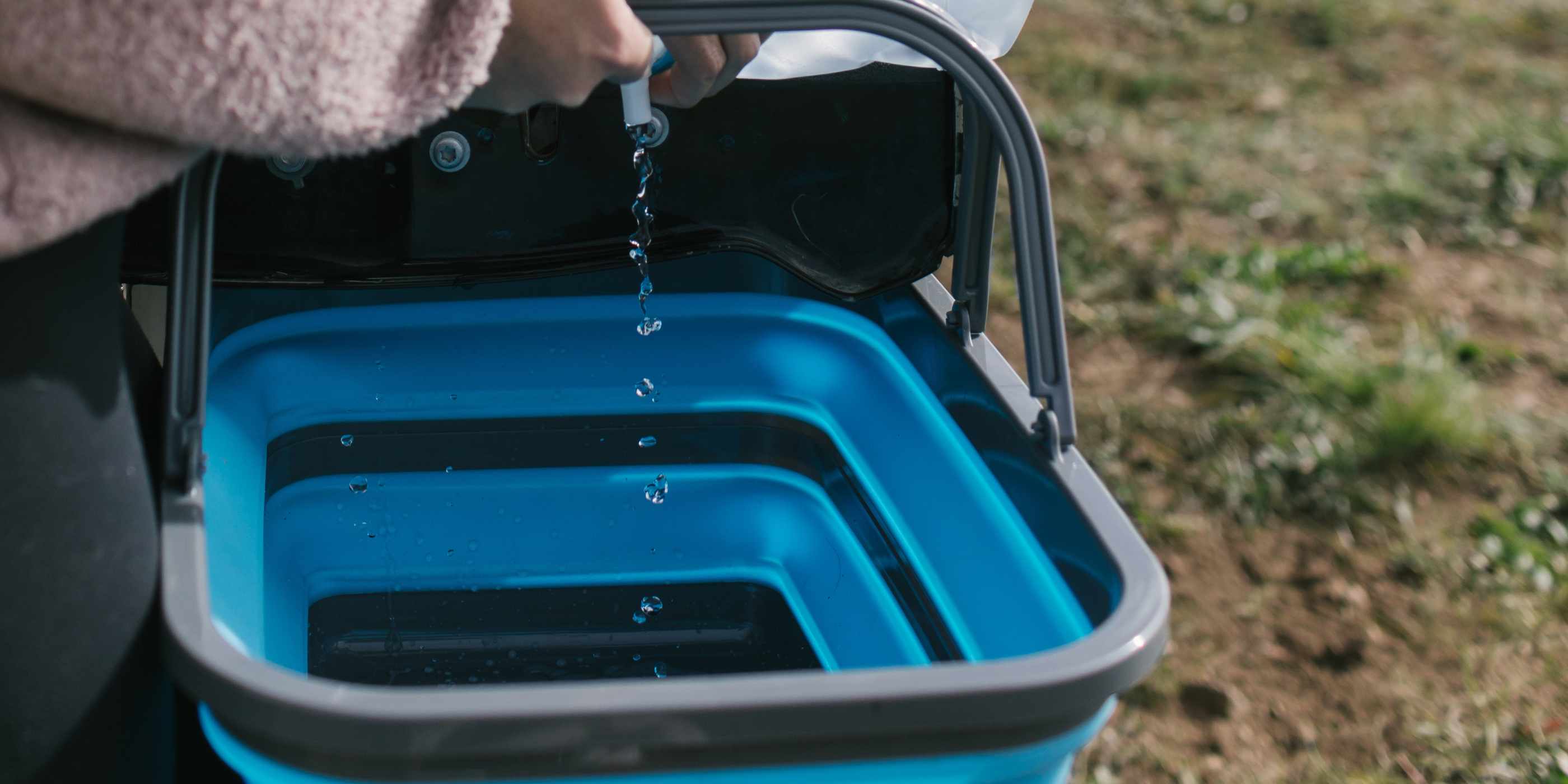 Woman Pouring Water into Blue and Gray SOL Flat Pack Collapsible Sink 16L