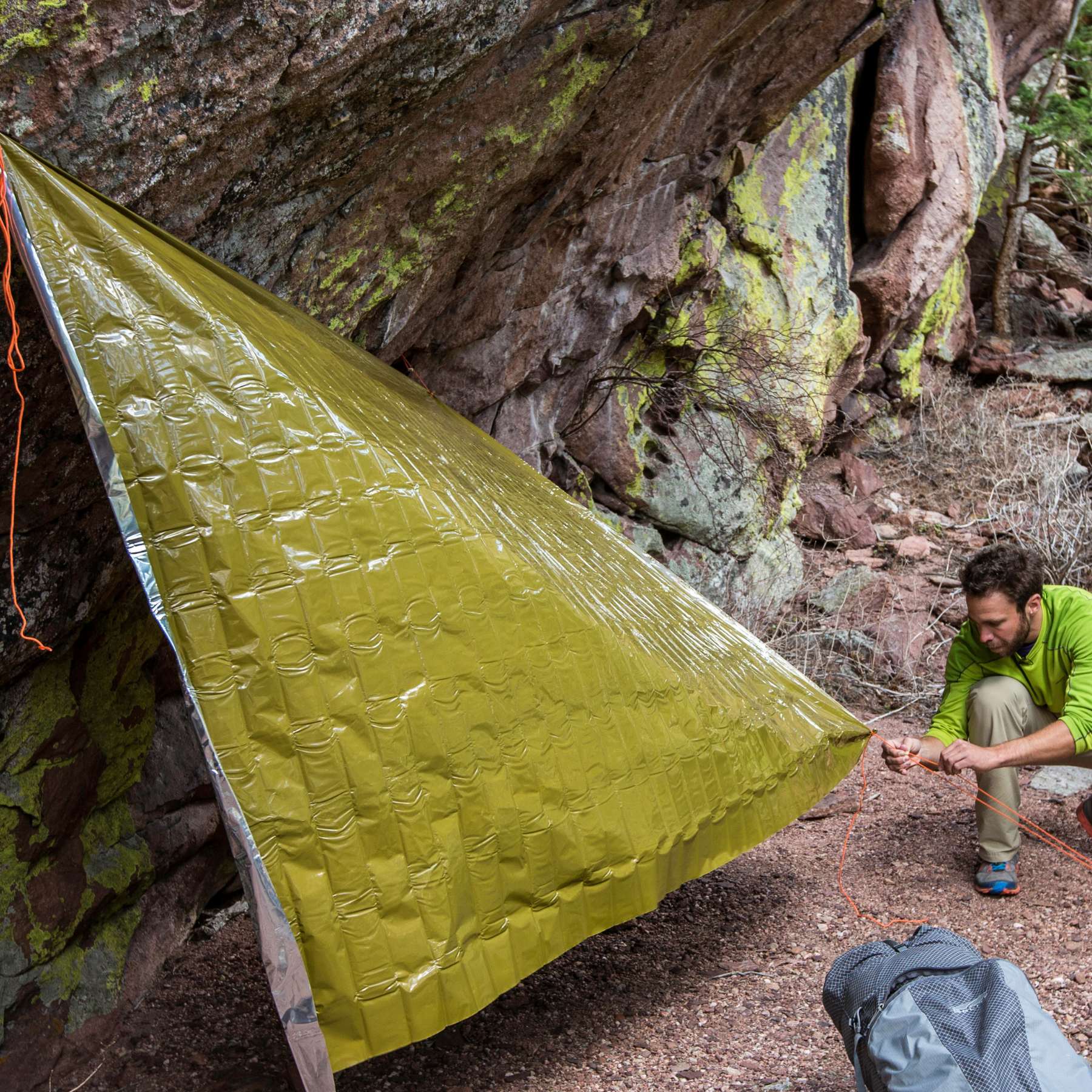 Man Rigging Green SOL Heavy Duty Emergency Blanket as a Shelter on a Large Rock