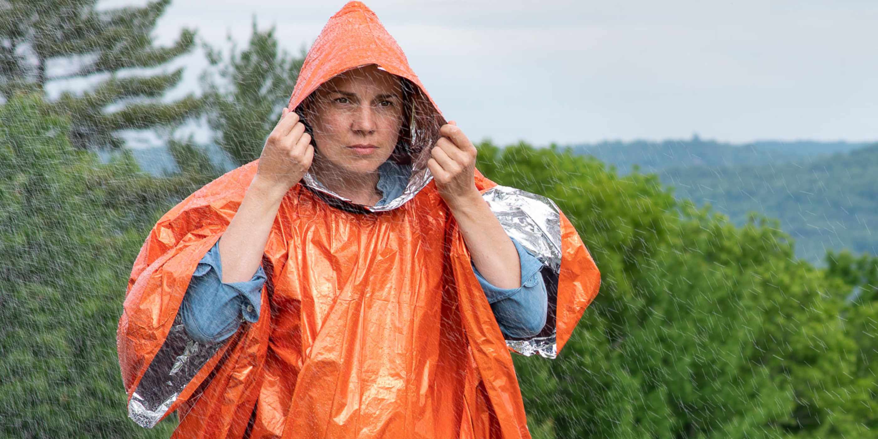 Woman in Orange SOL Heat Reflective Poncho in the Rain Against Mountain Background