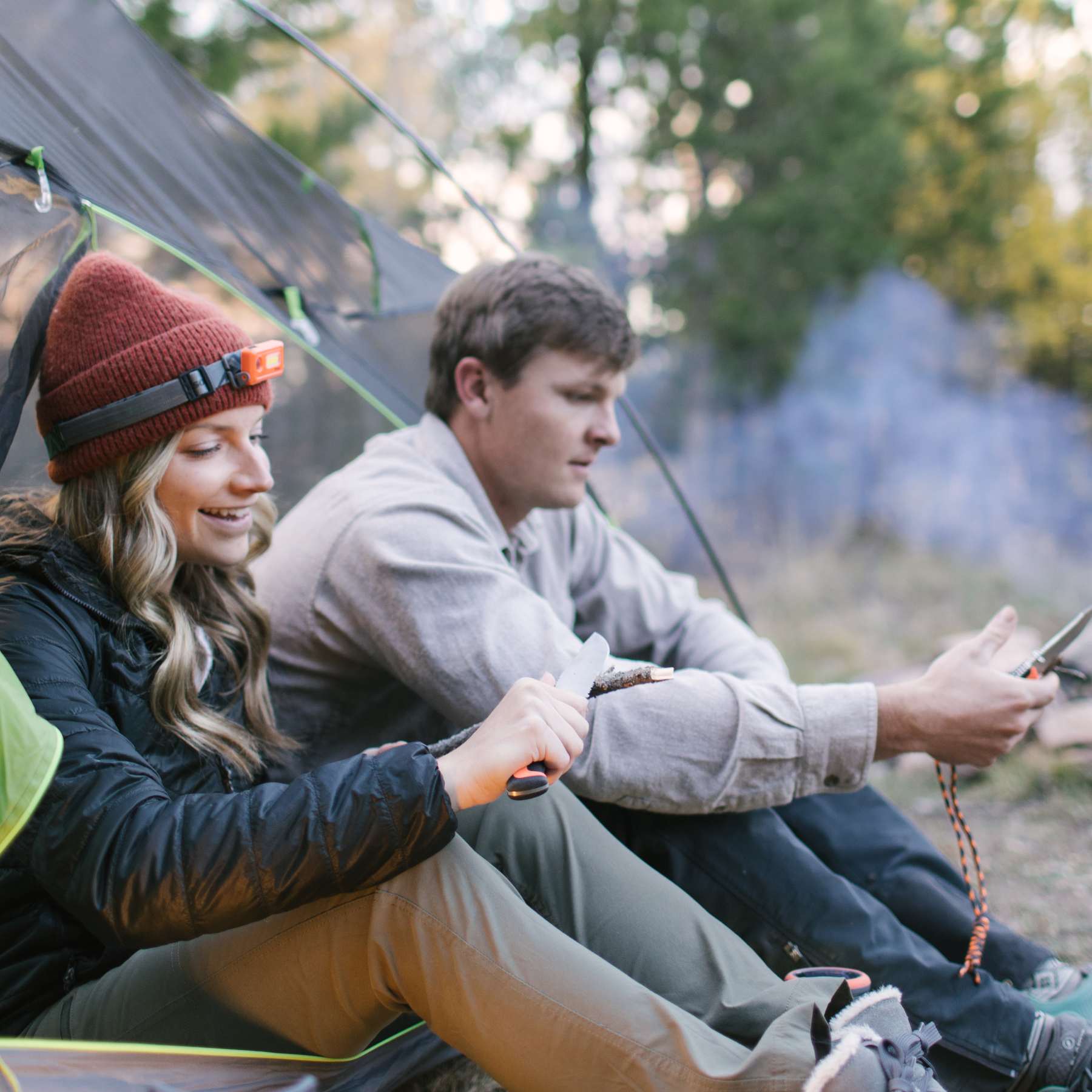 Two People in Tent Opening, Woman Wearing SOL Venture Headlamp on Red Hat
