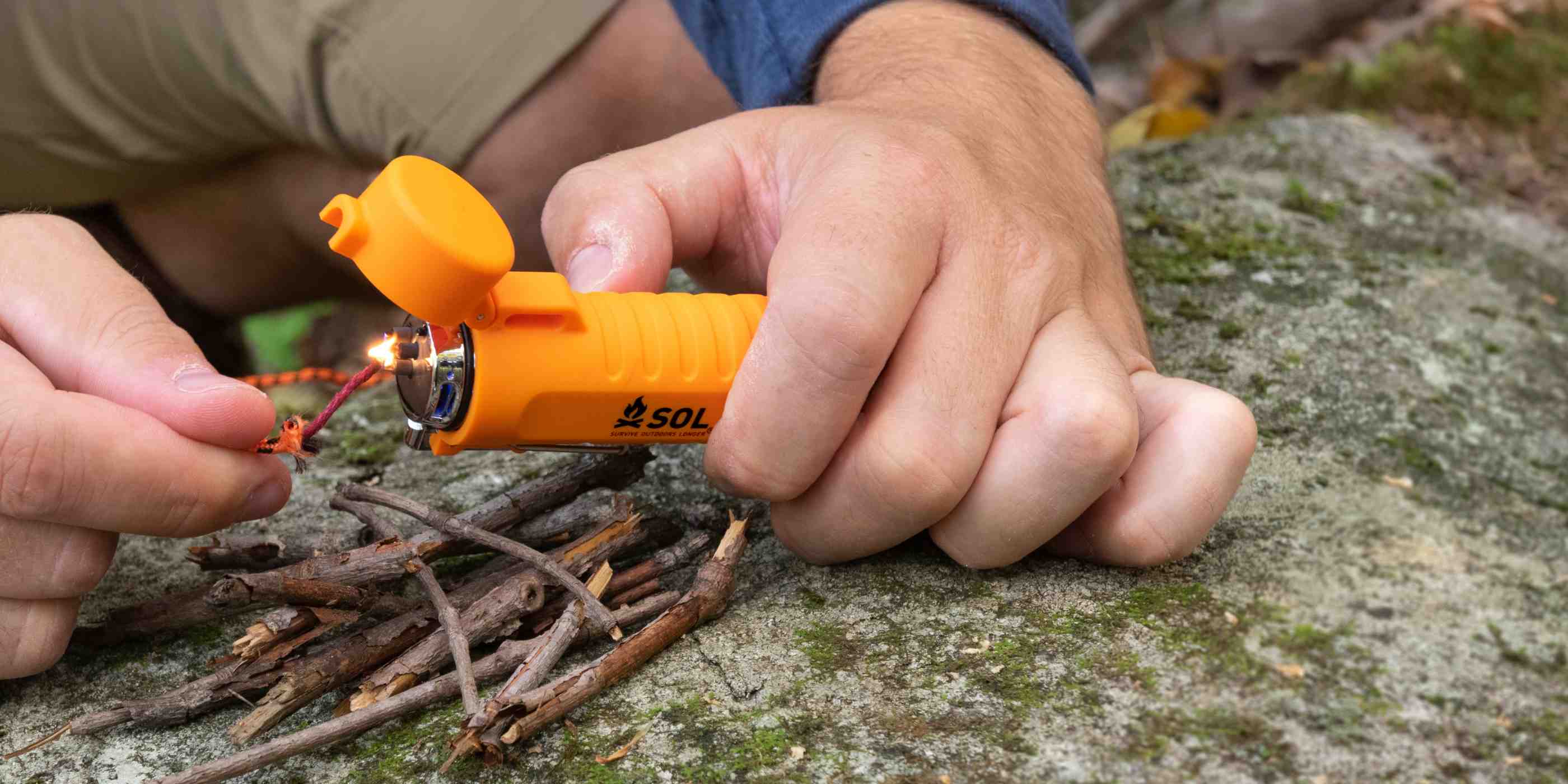 SOL Fuel Free Lighter being used to light tinder cord on rock showing reliable fire starting outdoor survival equipment