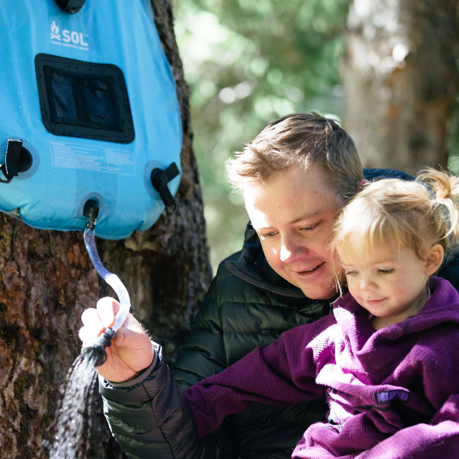 Father Using Blue Solar Shower Hanging on Tree with Daughter