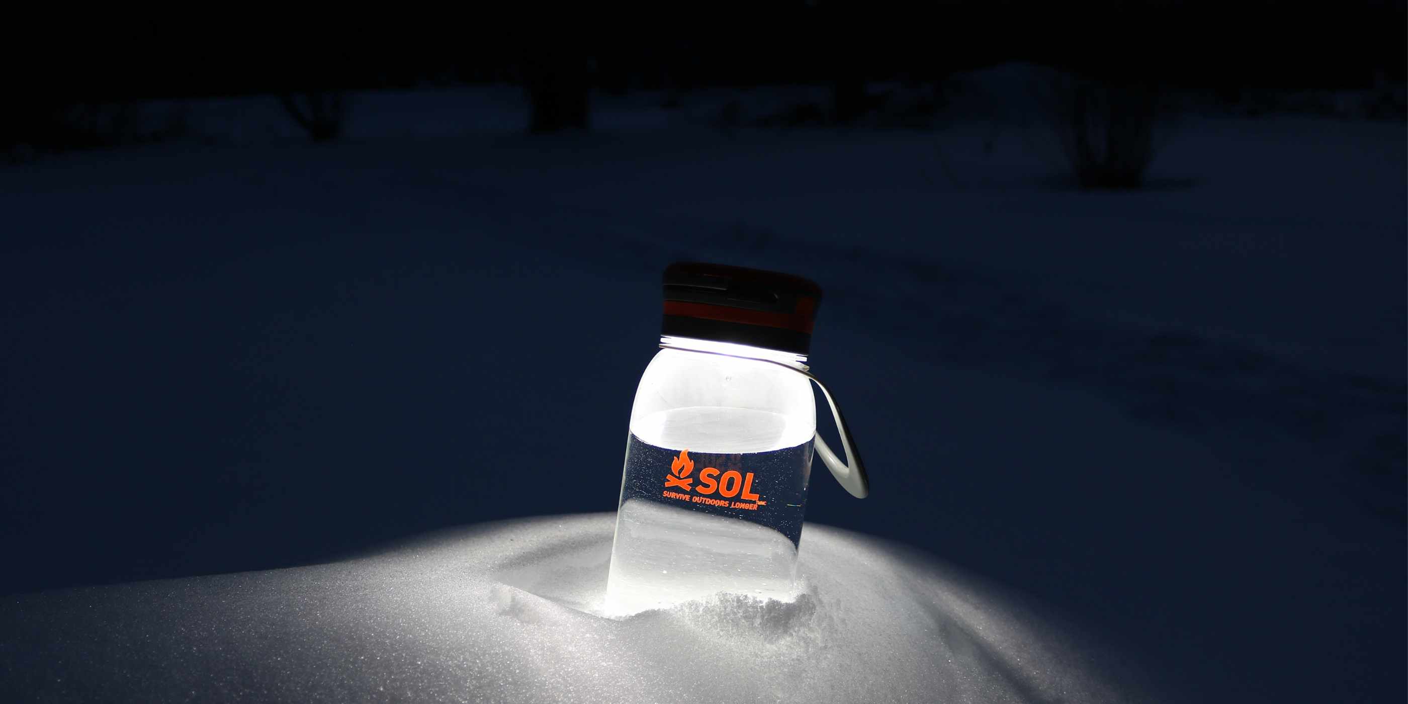 SOL Solar Water Bottle Lantern Lit Sitting in Snow in Darkness