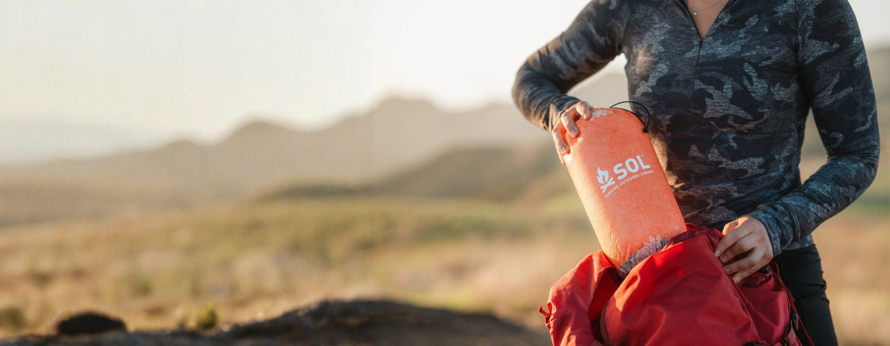 Woman in technical gear stuffing an SOL bivvy into her backpack
