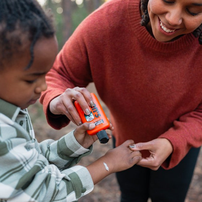 adult putting lotion on child outdoors