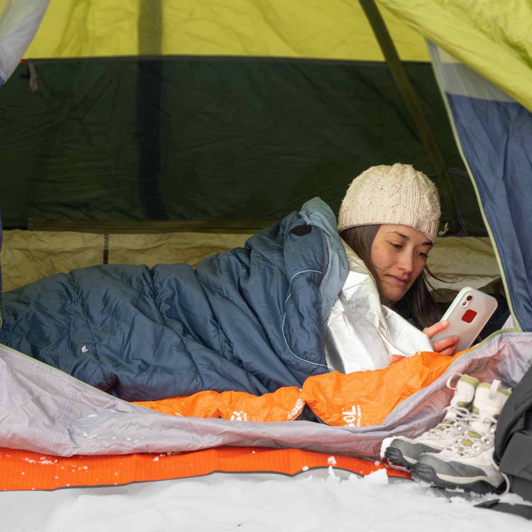 Thermal Bivvy with Rescue Whistle woman in tent with bivvy inside sleeping bag looking at phone in winter