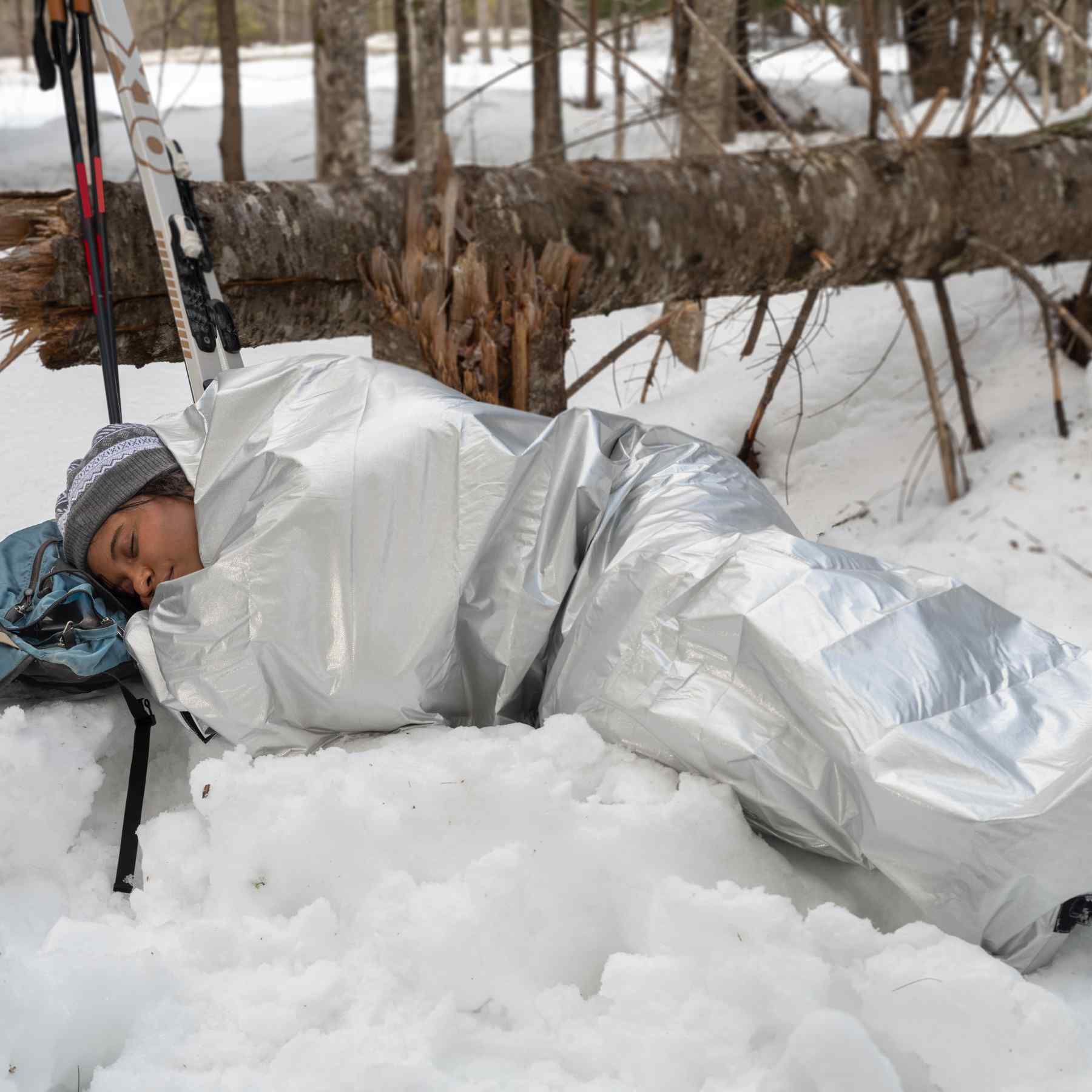 Thermal Bivvy with Rescue Whistle woman in bivvy laying in snow with head on backpack