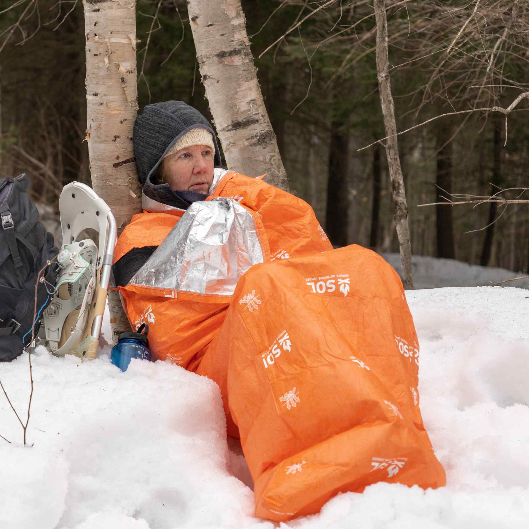 Escape Lite Bivvy woman in bivvy leaning on trees in snow with snowshoes next to her