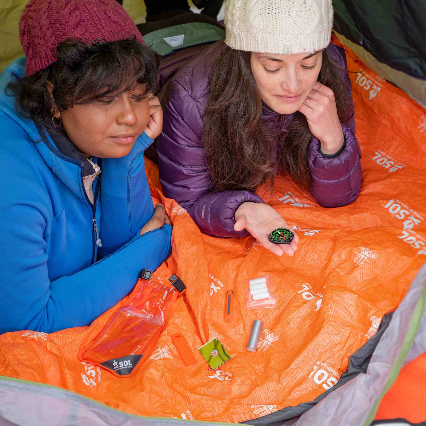 Scout Survival Kit two women inspecting contents of kit laying on orange SOL blanket