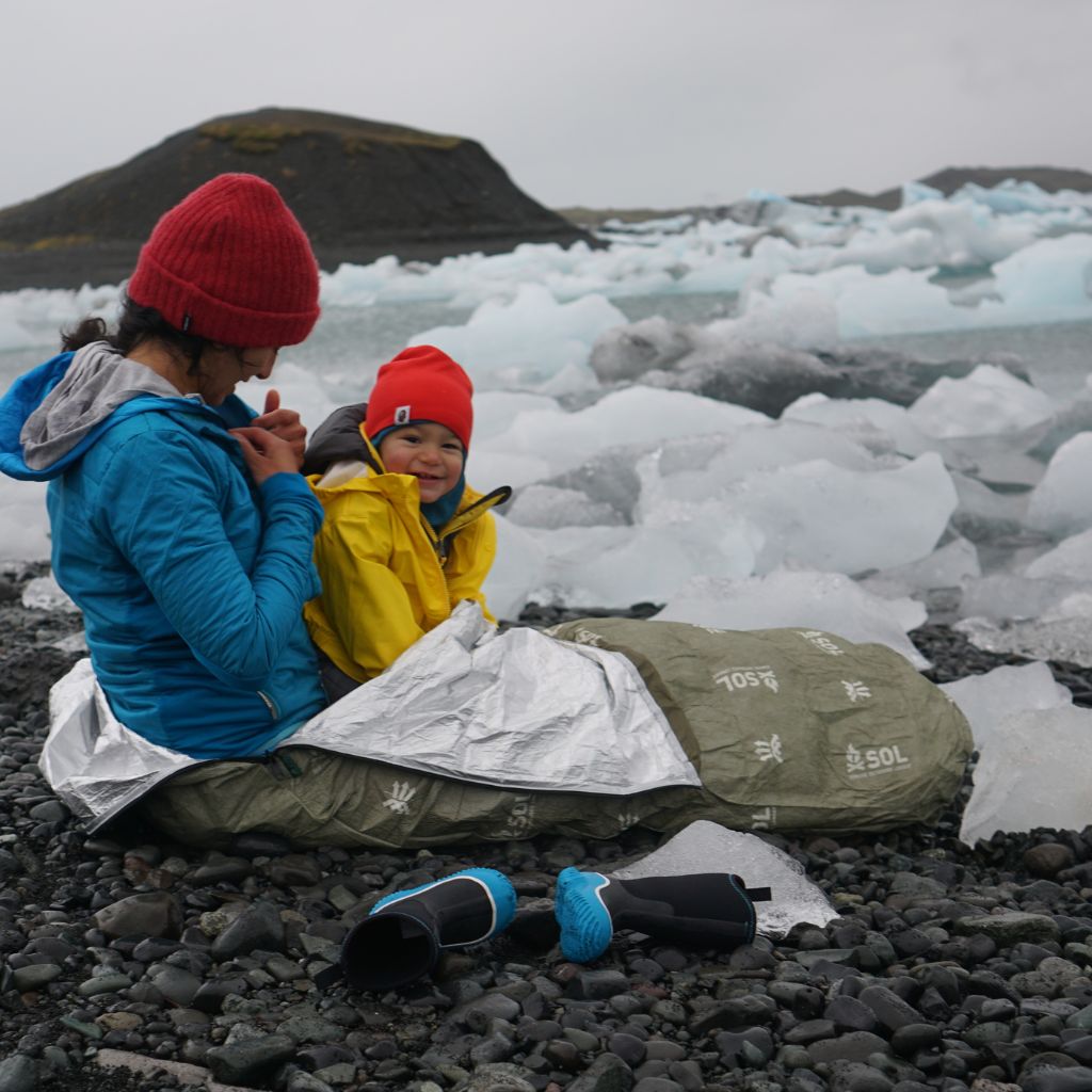 Escape Bivvy OD Green woman and child snuggled into bivvy on rocks near frozen water