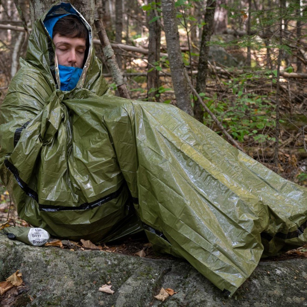Emergency Bivvy with Rescue Whistle - OD Green man wrapped in bivvy in the woods