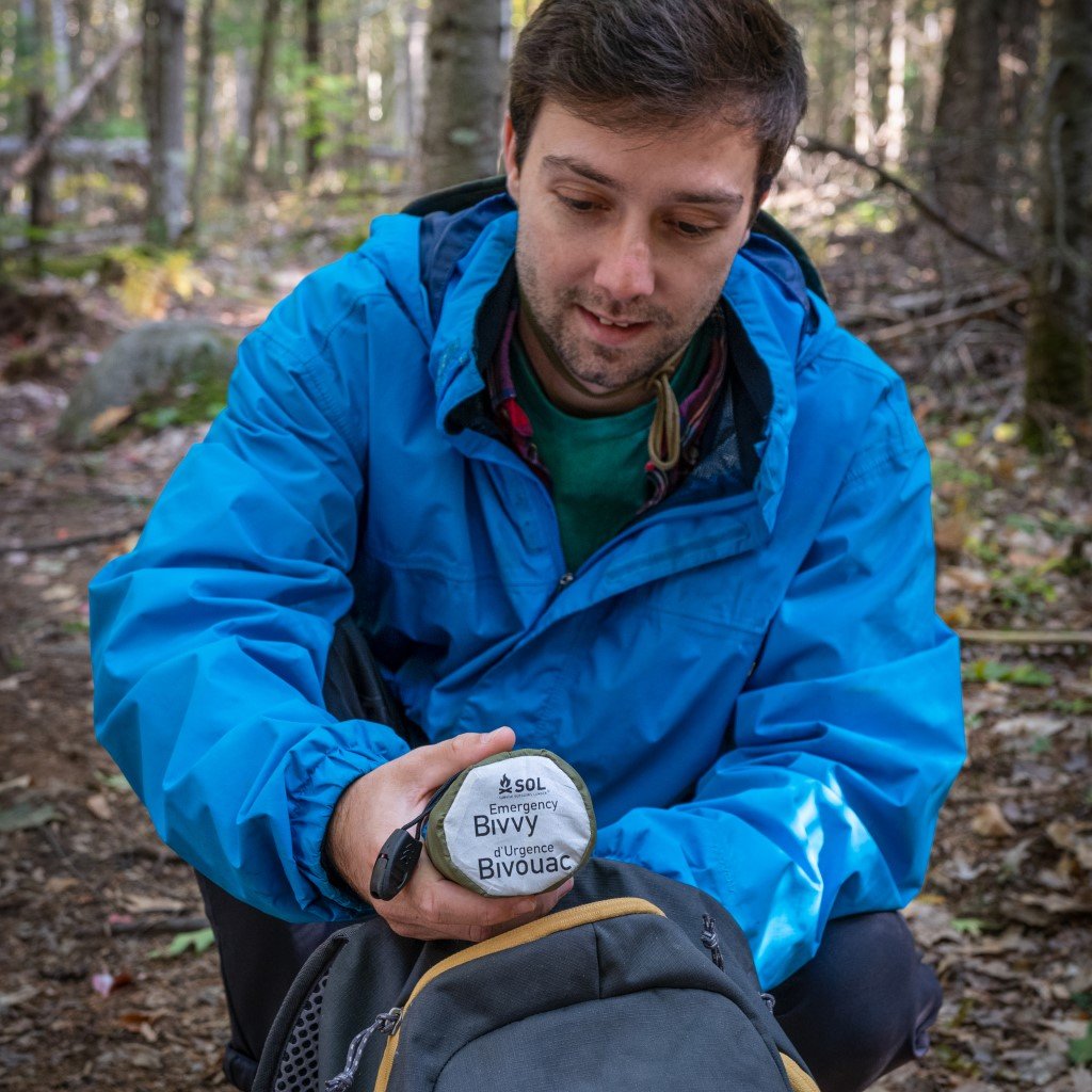 Emergency Bivvy with Rescue Whistle - OD Green man placing bivvy in sleeve into backpack