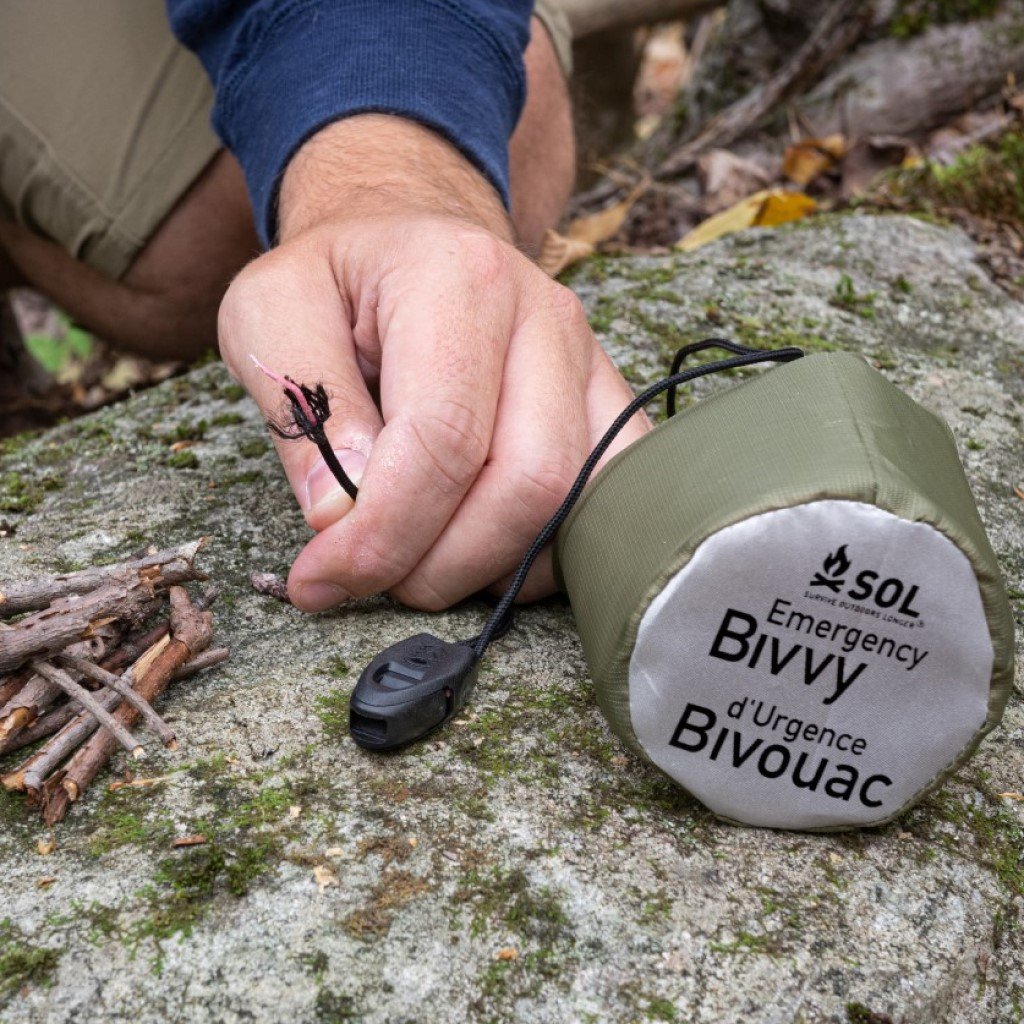 Emergency Bivvy with Rescue Whistle - OD Green using tinder cord to light fire on rock
