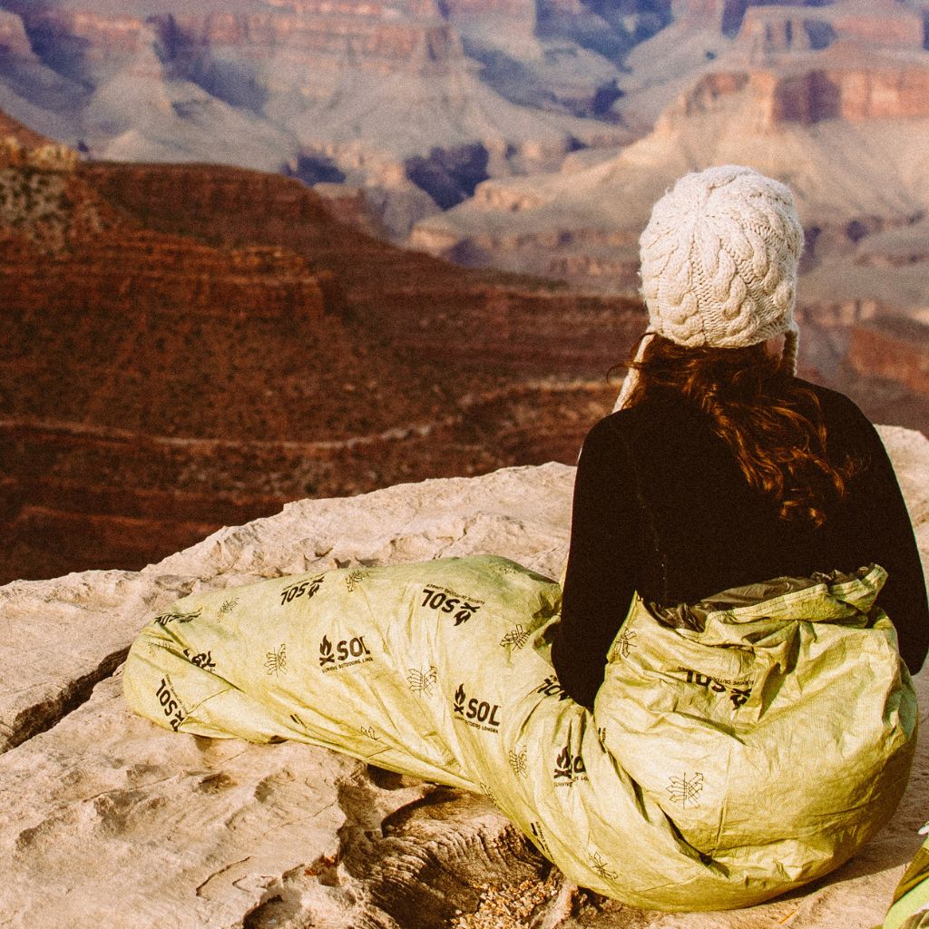 Escape Bivvy OD Green woman looking out at view while sitting on rocky surface in bivvy wearing hat