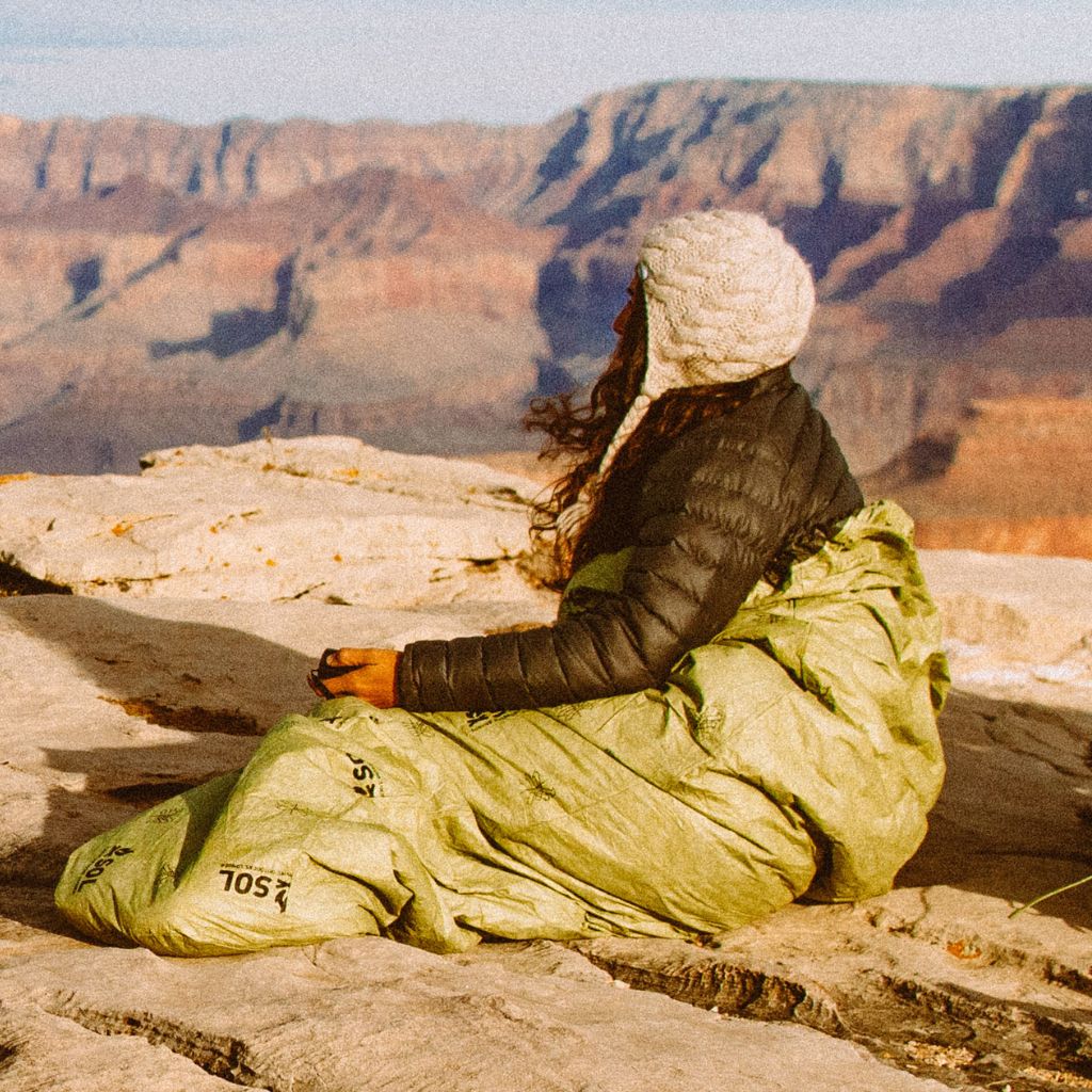 Escape Bivvy OD Green woman in hat and jacket sitting on rock in bivvy