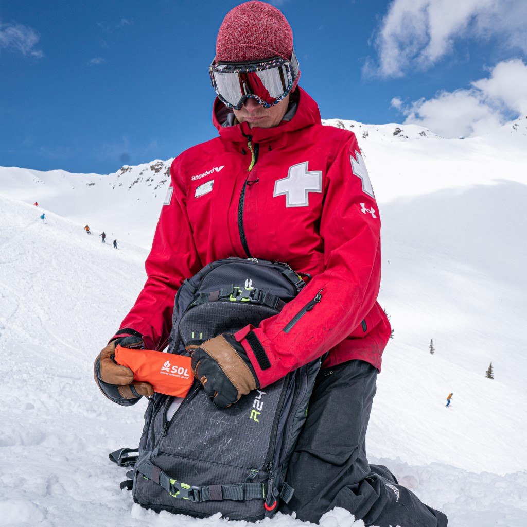 Emergency Bivvy with Rescue Whistle - Orange ski patrol pulling bivvy out of pack on snowy mountain