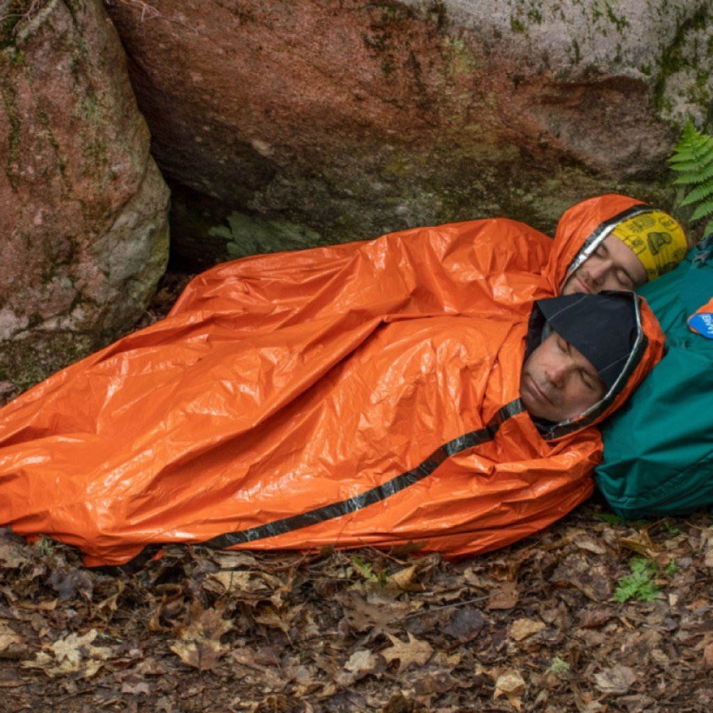 Emergency Bivvy XL w/ Rescue Whistle two people in bivvy sleeping with heads on green backpack on leaves in front of rock