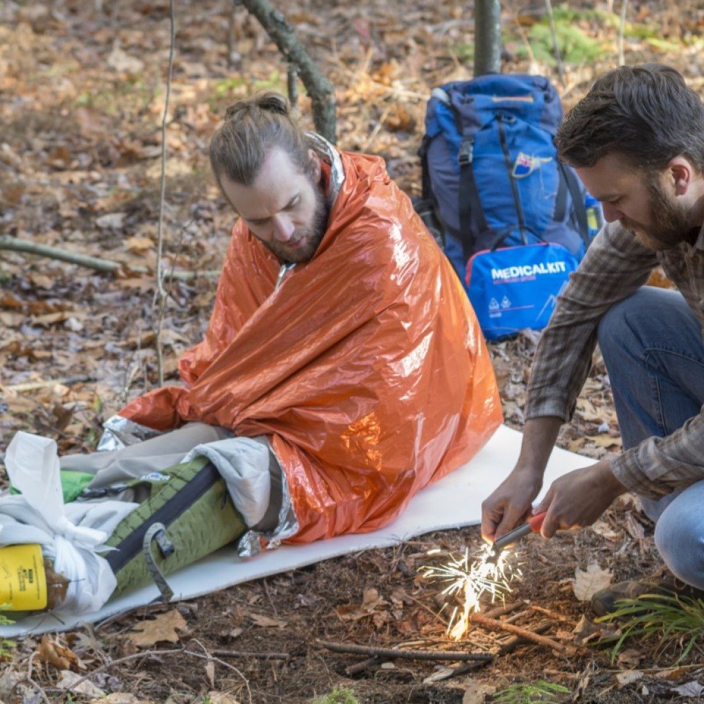 Emergency Blanket injured man wrapped in blanket next to man starting fire with Mag Striker creating sparks