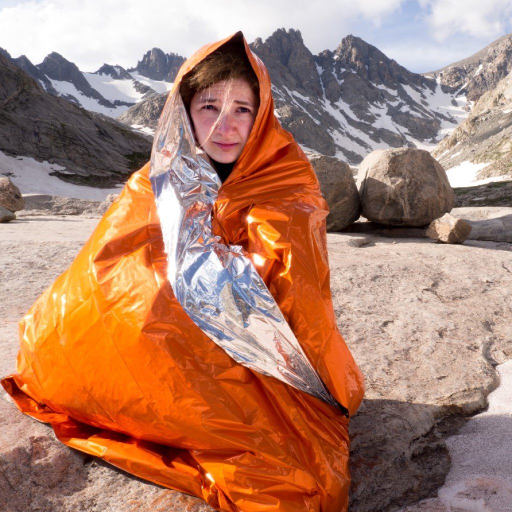 Emergency Blanket woman wrapped in blanket sitting on snowy rocks