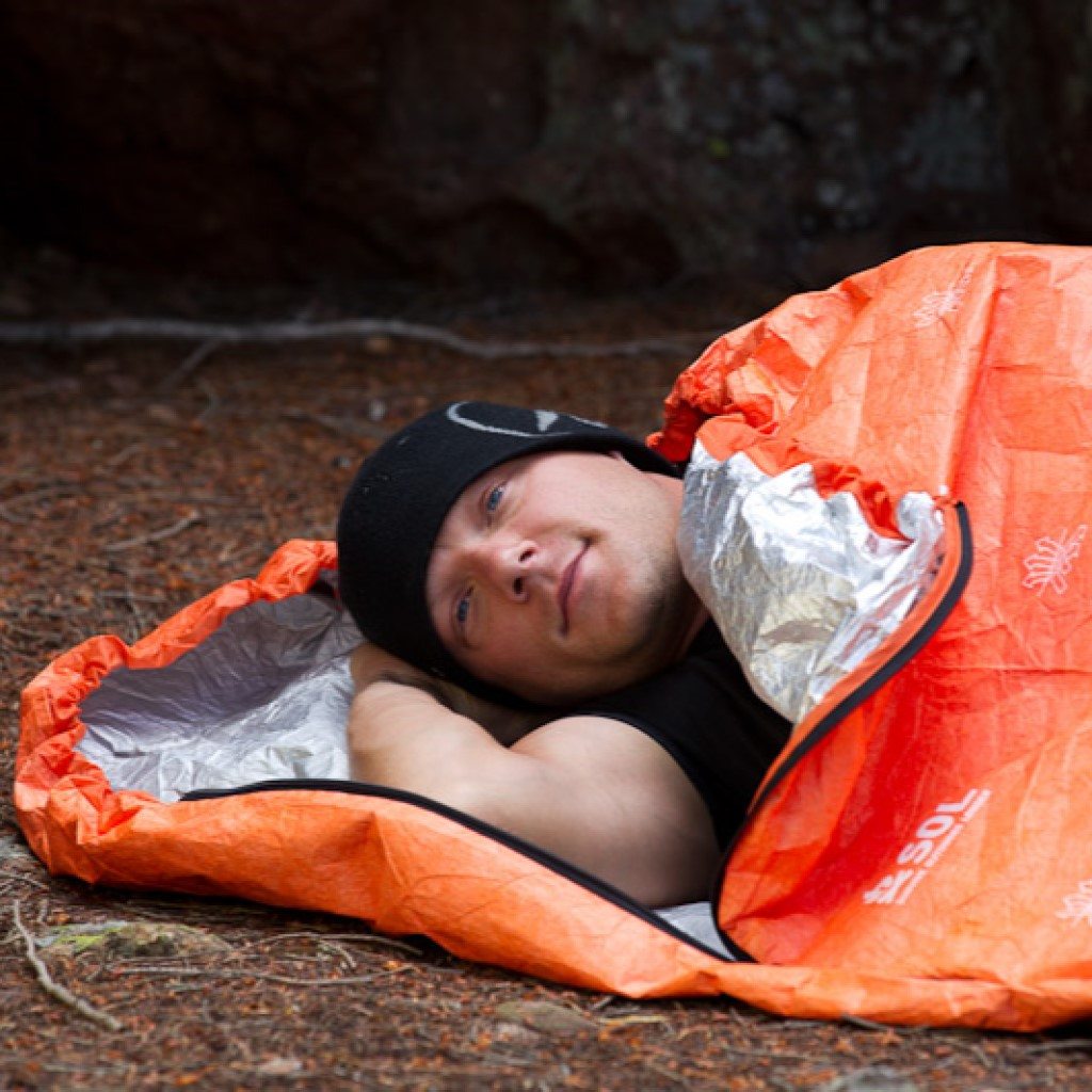 Escape Bivvy Orange man in black hat laying in bivvy on ground