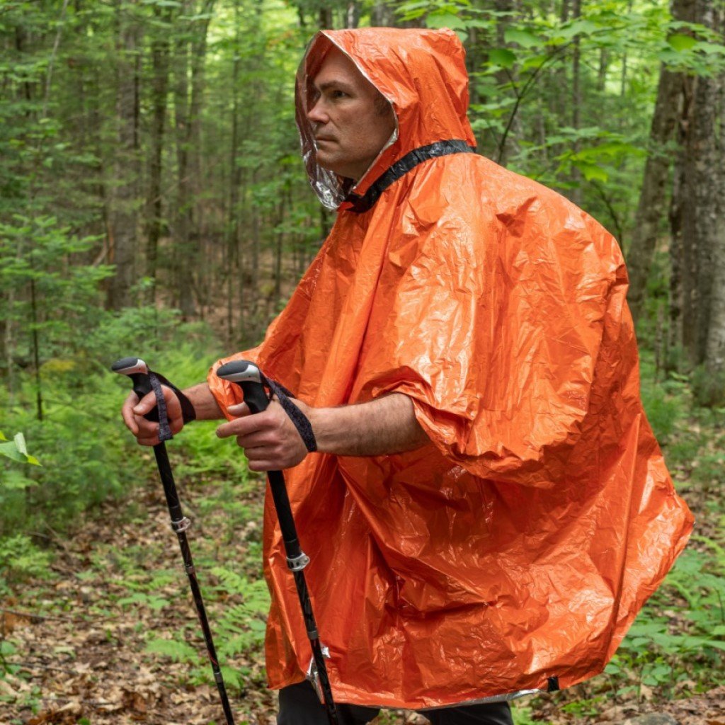 Heat Reflective Poncho man wearing poncho while hiking in the rain with hiking poles and backpack covered