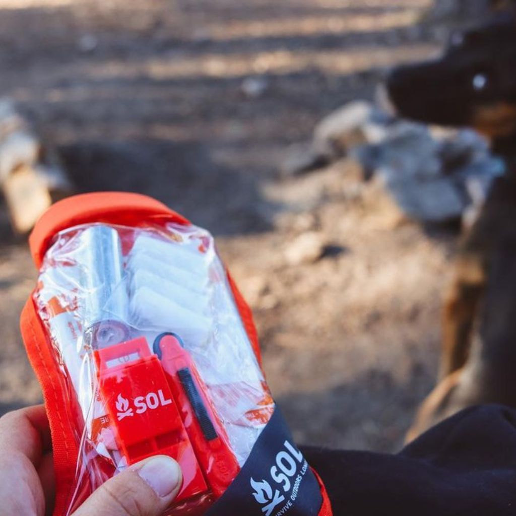 Scout Survival Kit holding kit in front of camping background and dog