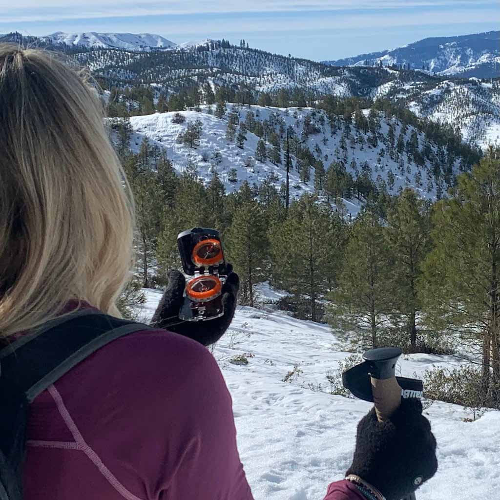 Sighting Compass with Mirror woman using on front of snowy mountains